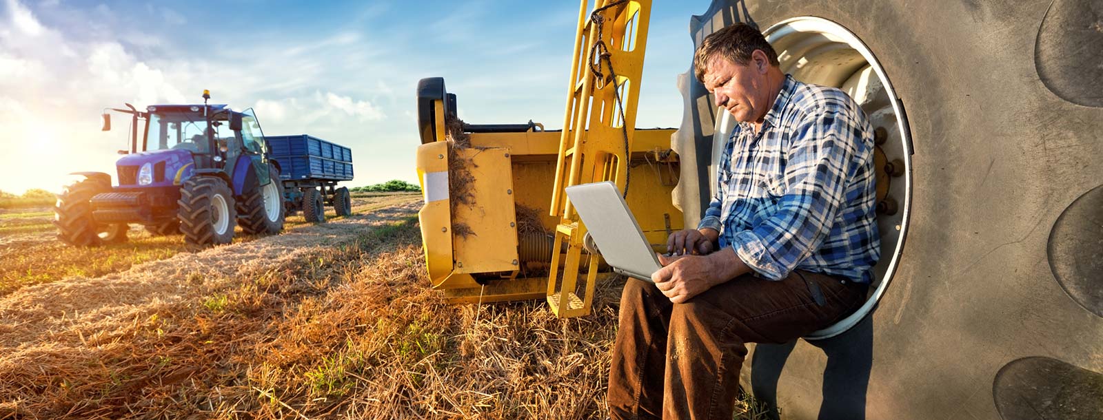A farmer on a laptop computer with his farming equipment